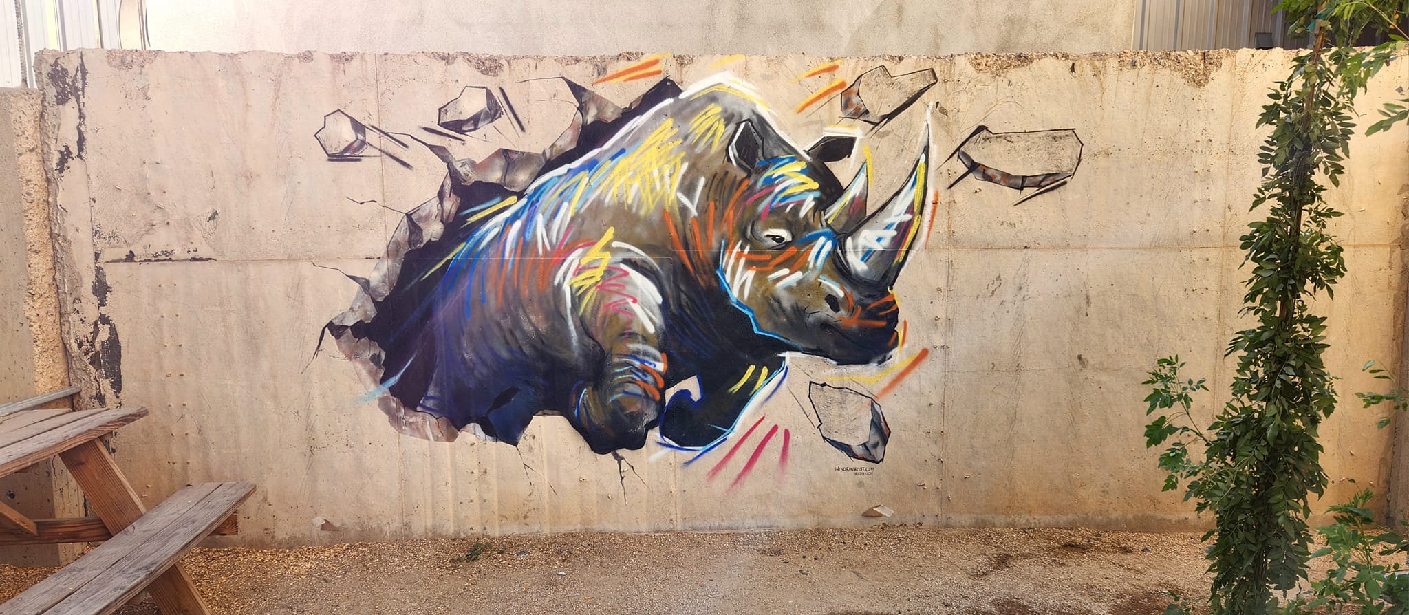 A rhino mural breaking through a concrete block wall, painted in black, white, blue, yellow, and red.